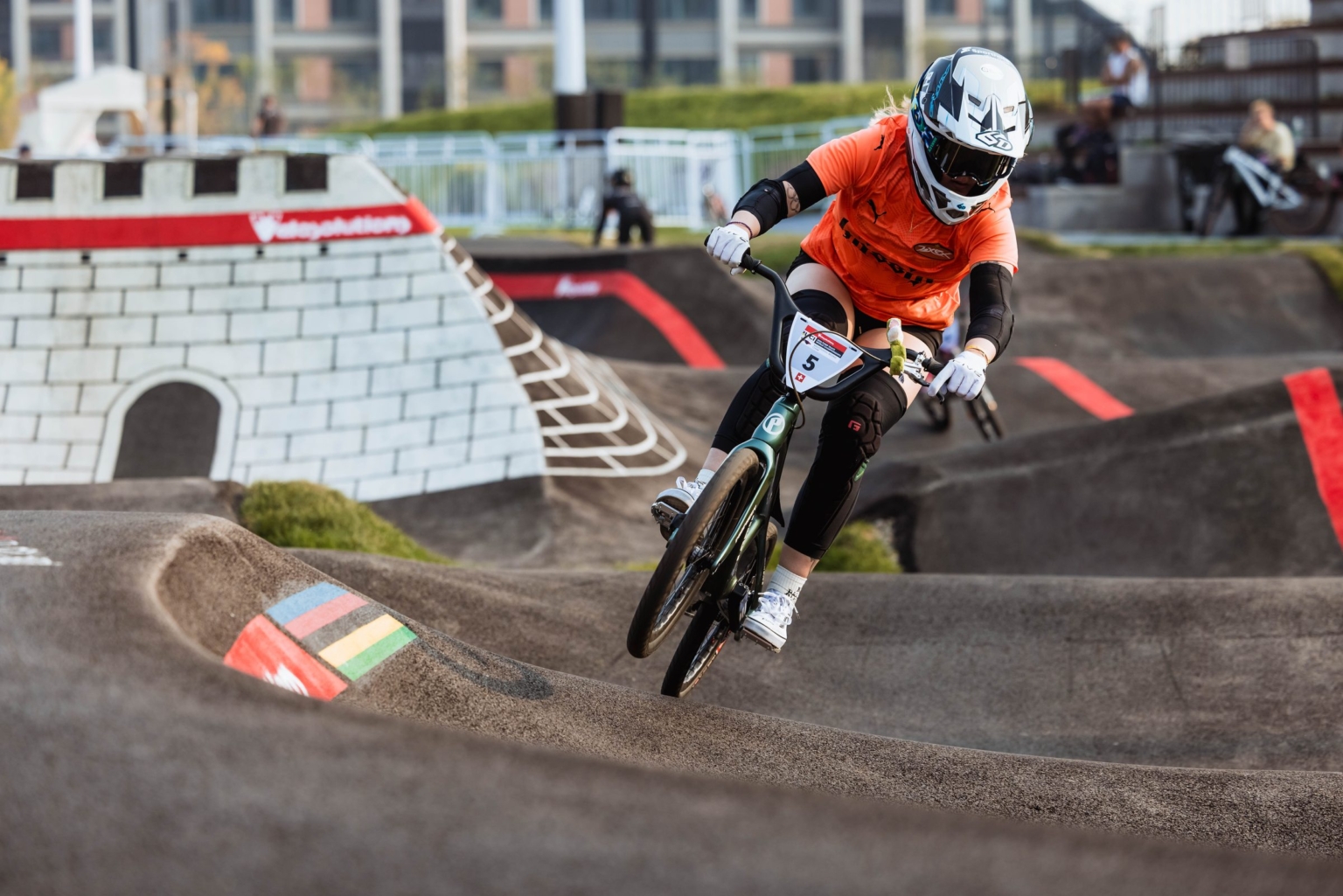 A rider in orange rolls through the rainbow-striped berm beside the Great Wall Towers in Mentougou