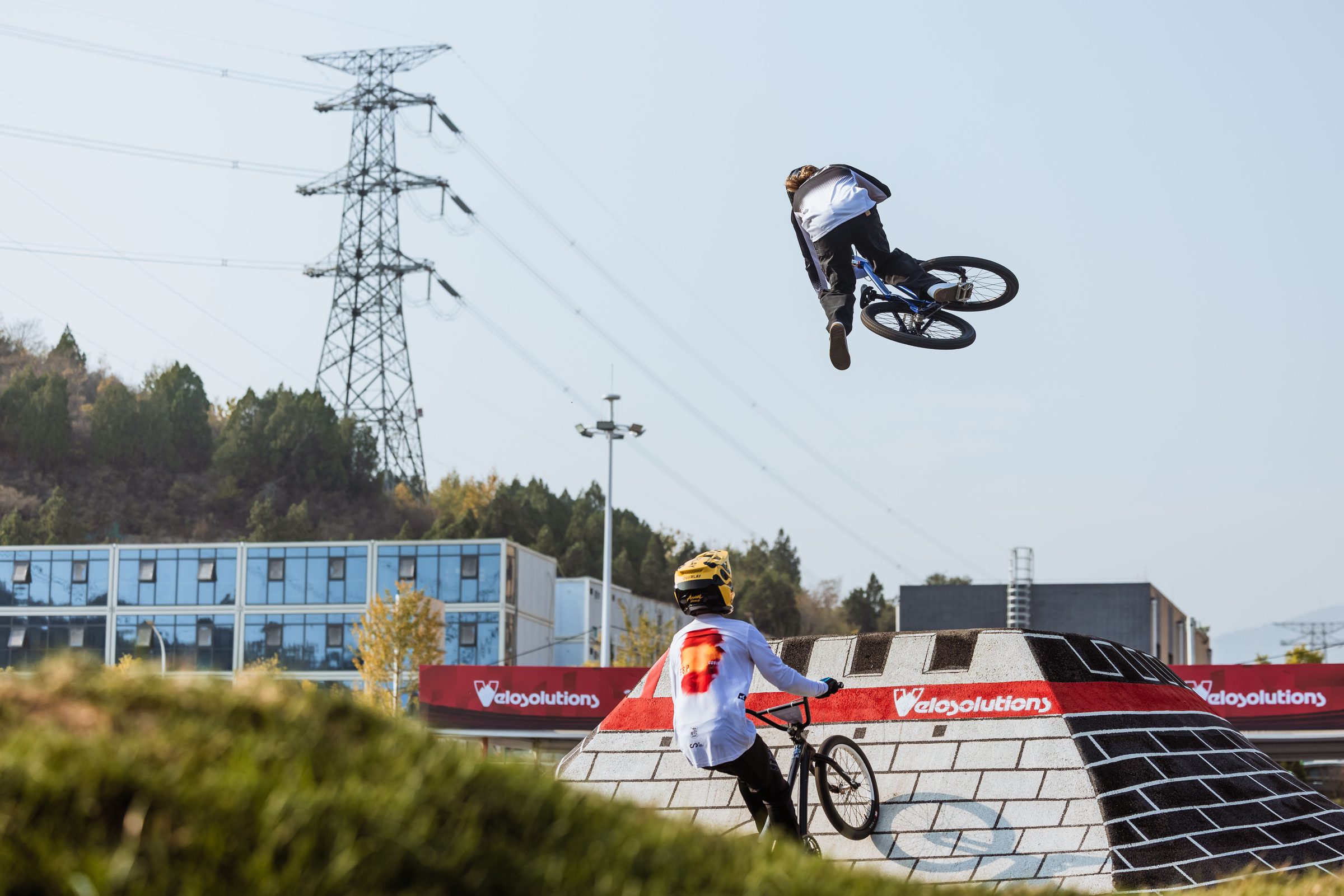 Two riders in the air above the Great Wall Towers at the Mentougou pump track